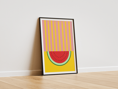 Framed abstract art print of a watermelon slice on a yellow background, leaning against a white wall.