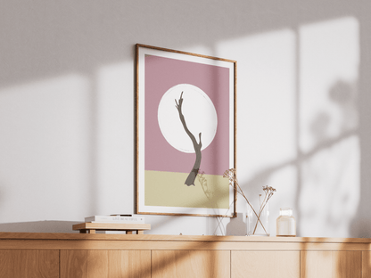 Framed artwork with a minimalist design of a Namibian tree silhouette against a pink background and white circle on a wooden surface.