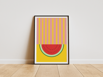 Framed abstract art print of a watermelon slice on a yellow background, leaning against a white wall.
