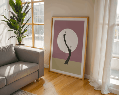 Framed artwork of a tree in Deadvlei in Namibia on a wall next to a gray sofa in a bright room with large windows.