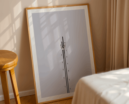 Framed winter skiing themed artwork on a wall with a wooden stool and bed in the foreground