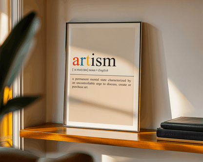 Framed dictionary definition of 'artism' on a shelf with books and a plant.