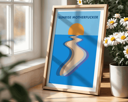 Framed artwork with a beach scene and 'Sunrise Motherfucker' text on a blue background, placed on a wooden surface with flowers.