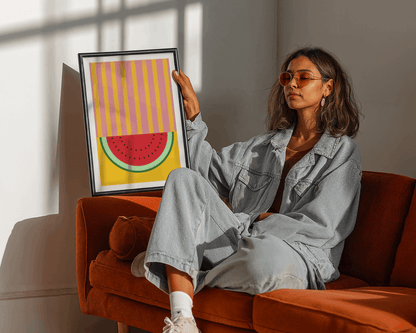 Woman holding a framed artwork of a watermelon on an orange couch.
