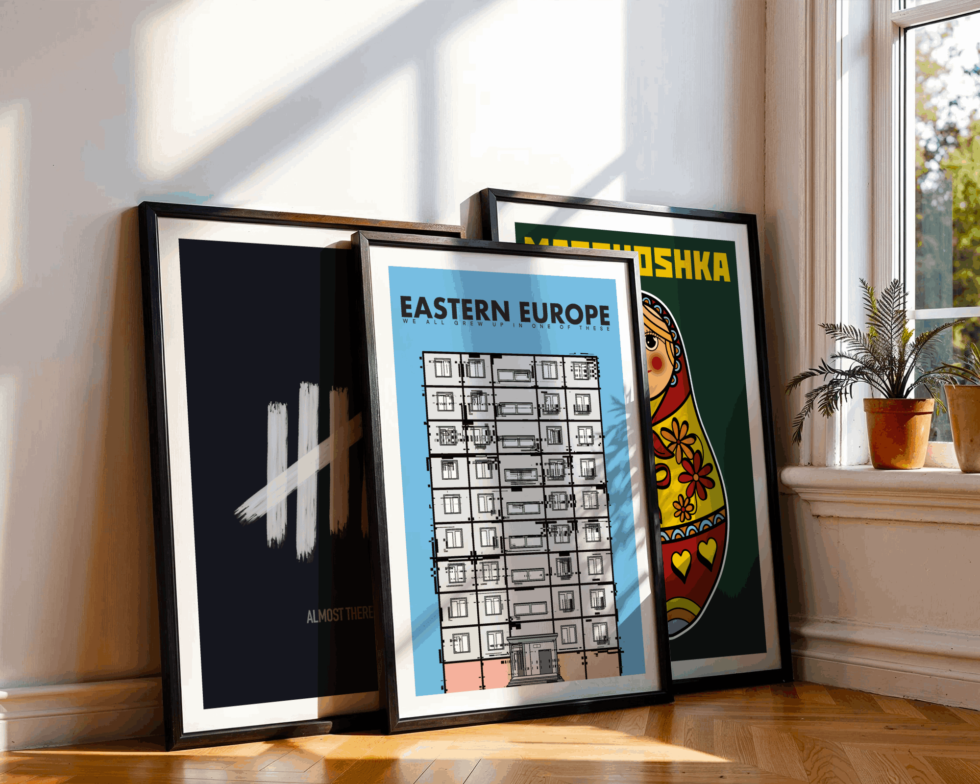Framed artworks on the floor with a window and plants in the background