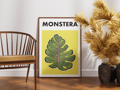 Framed plant poster with 'MONSTERA' on a wall next to a wooden chair and decorative plant.