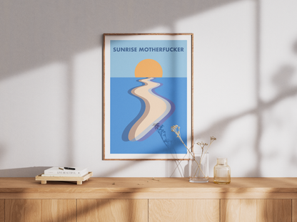 Framed artwork with a sunset and 'SUNRISE MOTHERFUCKER' text on a white wall above a wooden cabinet.